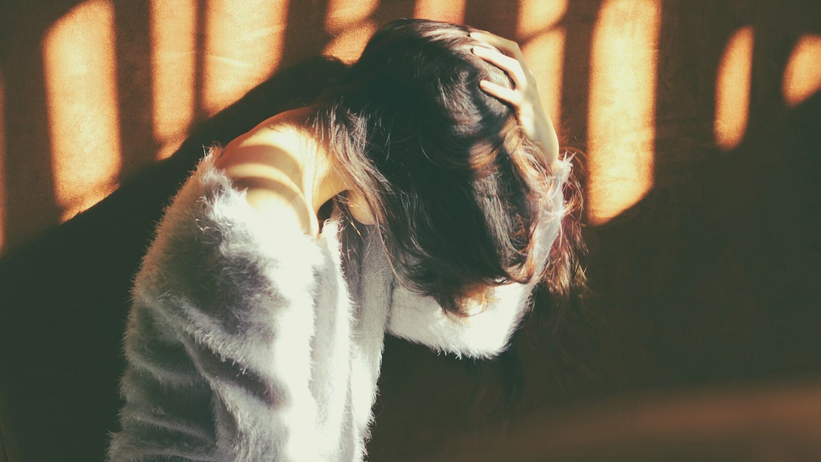 woman leans on wall in white fur jacket docking her head while holding it using her leaf hand