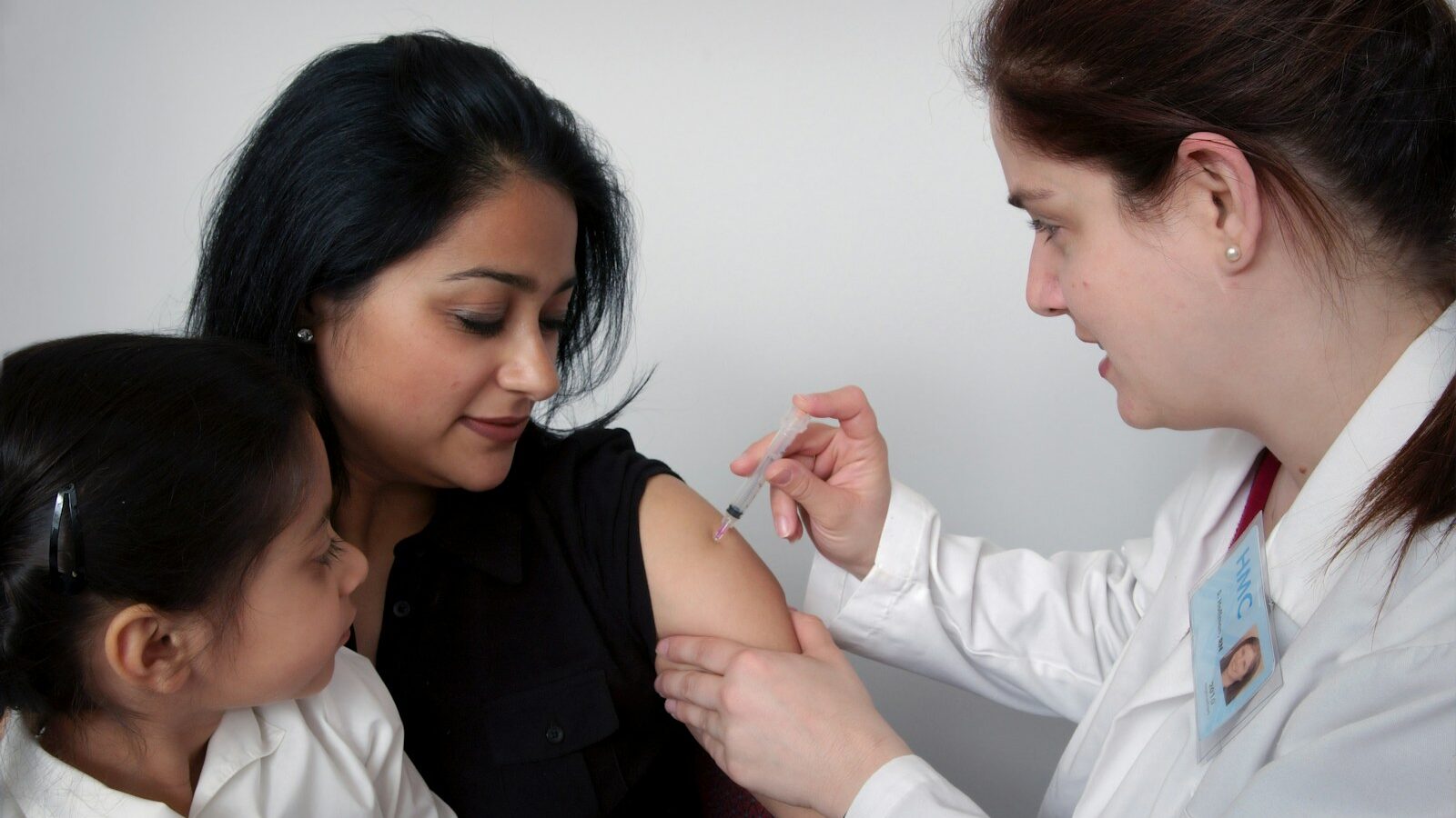 woman injecting woman's arm carrying child